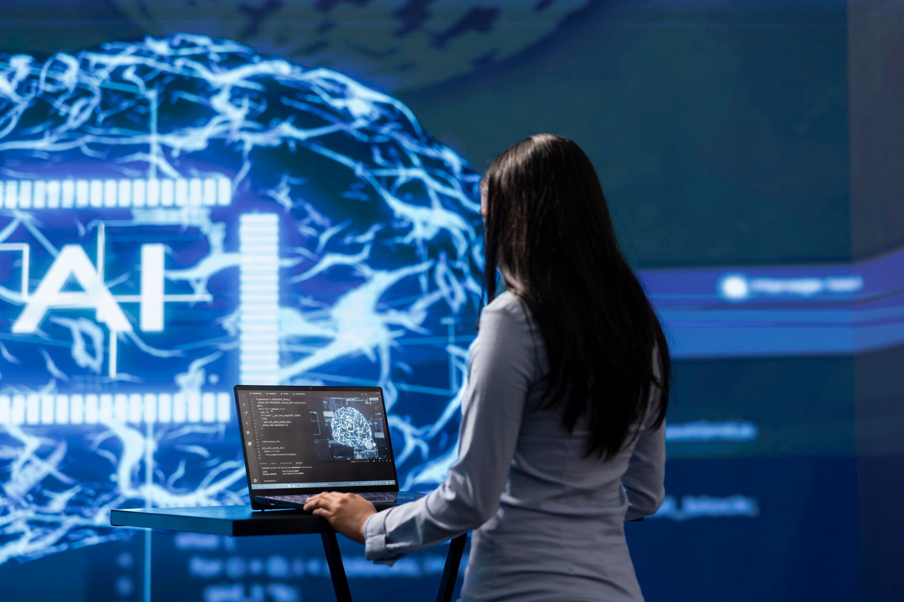 A woman in a white shirt interacts with a laptop displaying AI coding, against a high-tech blue brain graphic backdrop.