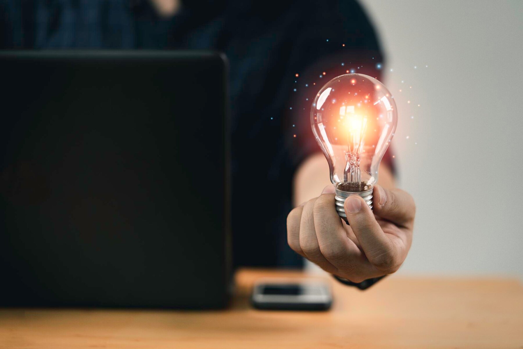 A person holding a glowing light bulb in front of a laptop, symbolizing creativity and innovative ideas.