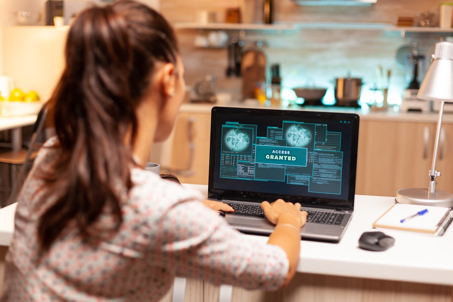 A woman with long, dark hair sits at a desk, focused on a laptop screen displaying