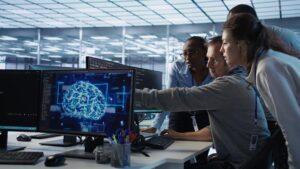 A group of professionals collaborates in a modern office, looking at a computer screen displaying a digital brain graphic labeled "AI."