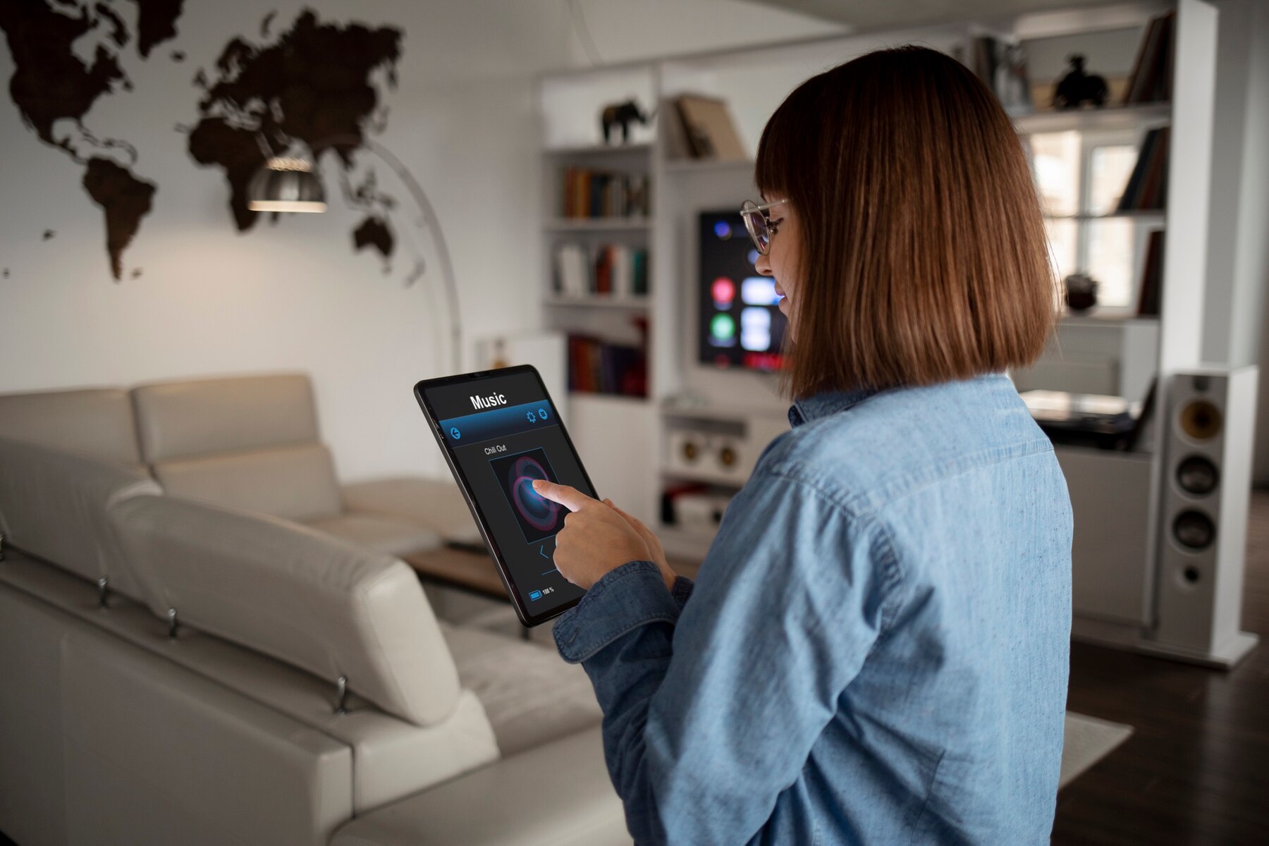 A person stands in a modern living room, using a tablet to control music, with a world map and stylish furniture in the background.