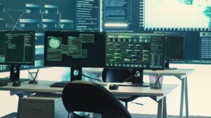 A high-tech workspace featuring multiple monitors displaying complex data analytics, network diagrams, and coding interfaces, with a sleek chair.
