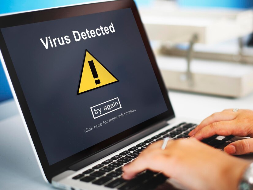 A person types on a laptop displaying a Virus Detected warning with an exclamation mark.