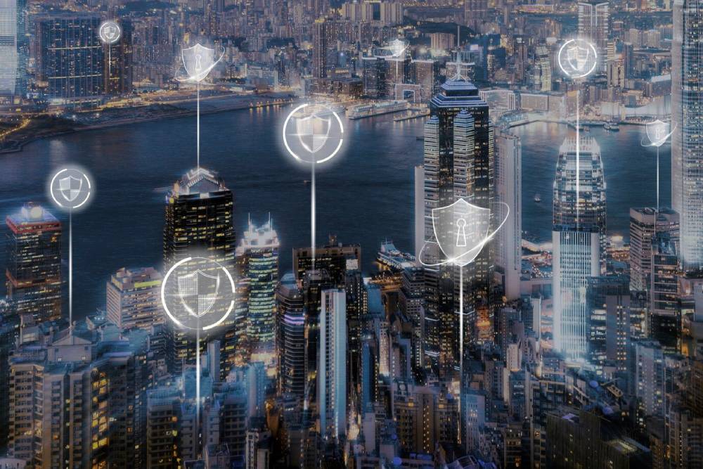 Aerial view of a smart city at night, overlaid with glowing cybersecurity icons, symbolizing digital protection.