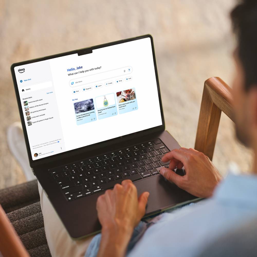 A person sitting in a chair types on a laptop displaying an Alexa help page with options and recent questions.