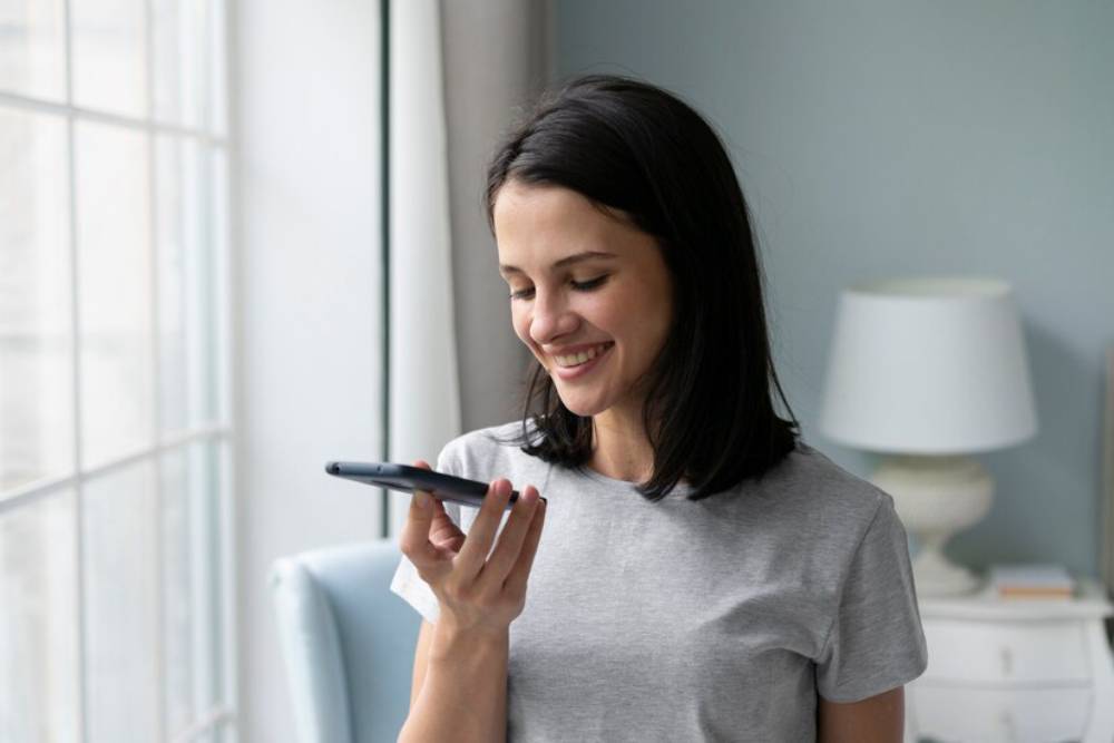 A person in a gray t-shirt holds a smartphone and use voice controlled assistant.