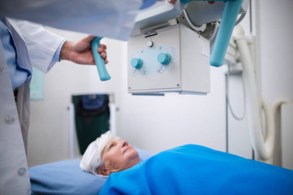 A healthcare professional doing robotic surgery above a patient lying on an examination table, covered with a blue sheet.