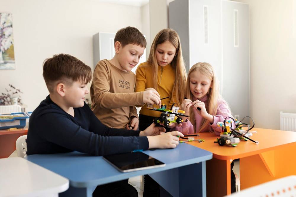 Children collaborate on a robotics project at colorful desks, engaging with materials and technology in a bright classroom.